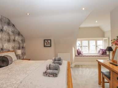 A bedroom with a bed, window seat with cushions, desk, and floral wallpaper at Rossett Holme in Ambleside