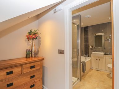 A wooden dresser with flowers and decorative items next to a bathroom with a shower tub sink and toilet at Rossett Holme in Ambleside