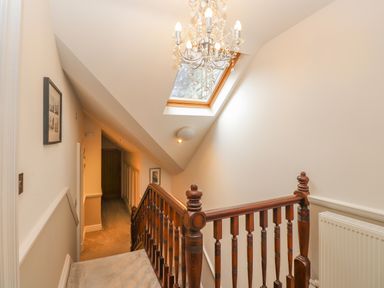 A hallway with a wooden staircase railing a skylight and a chandelier at Rossett Holme in Ambleside