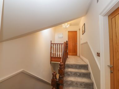 A carpeted staircase with wooden banisters leading to a hallway with wooden doors and a chandelier at Rossett Holme in Ambleside