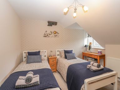 A bedroom with two single beds a wooden bedside table and a wooden desk under a sloped ceiling at Rossett Holme in Ambleside