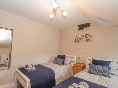 A bedroom with two single beds a wooden nightstand and a wall mirror at Rossett Holme in Ambleside
