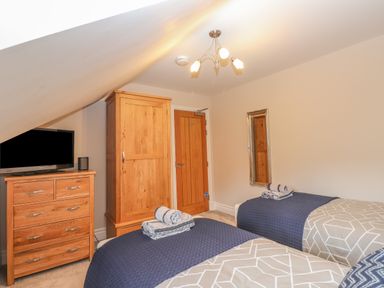 A bedroom with two single beds with folded towels on them a wooden wardrobe a chest of drawers with a television and a wall mirror at Rossett Holme Ambleside