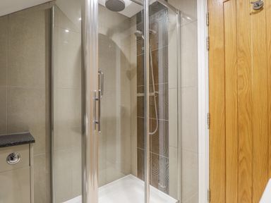 A shower with glass doors next to a wooden door in a bathroom at Rossett Holme in Ambleside