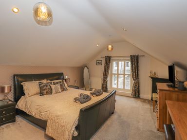 A bedroom with a double bed side tables a dressing mirror a window with curtains a chest of drawers and a television at Rossett Holme Ambleside
