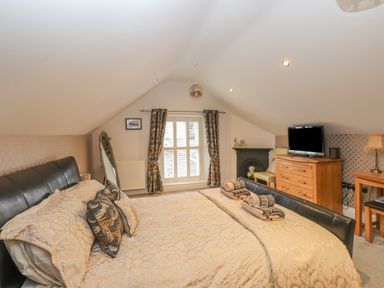A bedroom with a large bed a wooden dresser TV window with curtains and a small fireplace at Rossett Holme in Ambleside