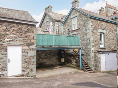 An exterior view of stone buildings with a covered parking area and stairs leading to a balcony at Rossett Holme in Ambleside