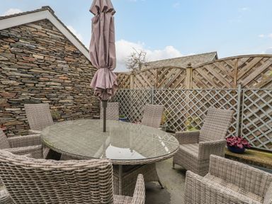 An outdoor patio with a glass top table surrounded by wicker chairs and a closed umbrella at Rossett Holme Ambleside