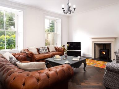 A living room with brown leather sofas a black coffee table a wood stove and a television at Ben House in Grasmere