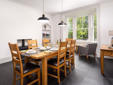 A dining room with a wooden table set for six and a gray armchair by the window at Ben House in Grasmere