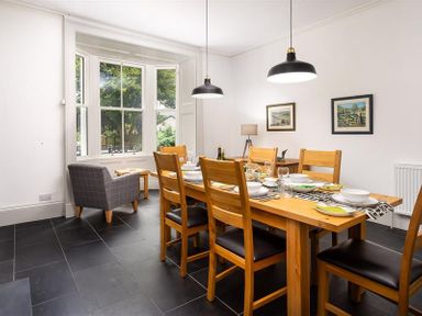 A dining room with a wooden table set for six and a gray armchair near a large window at Ben House in Grasmere