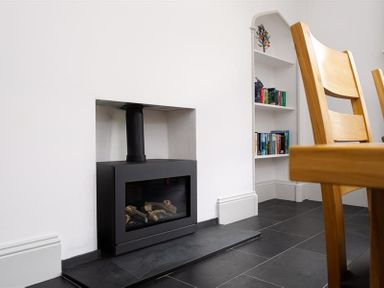 A black fireplace with logs inside a white wall next to a built-in white bookshelf and wooden chairs at Ben House in Grasmere