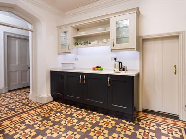 A kitchen area with black lower cabinets beige upper cabinets a kettle and fruit bowl on the counter and patterned tile floor at Ben House in Grasmere