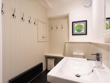 A bathroom with a sink toilet wall hooks radiator and framed artwork at Ben House in Grasmere