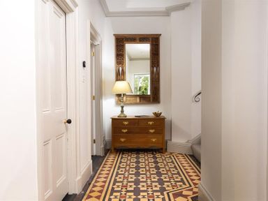 A hallway with patterned tile floor a wooden chest of drawers a table lamp and a wall mirror at Ben House in Grasmere