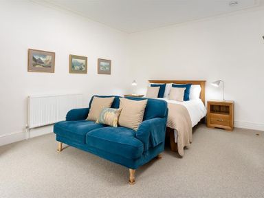 A bedroom with a blue sofa a wooden bed with blue and beige pillows and wooden nightstands at Ben House in Grasmere