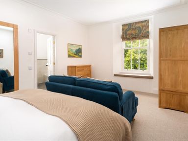A bedroom with a bed a blue sofa wooden dresser wardrobe window and a door at Ben House in Grasmere