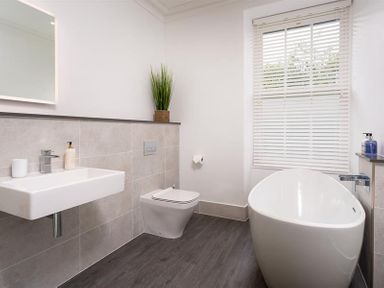 A bathroom with a white sink, toilet, freestanding bathtub, window blinds, and a potted plant at Ben House in Grasmere
