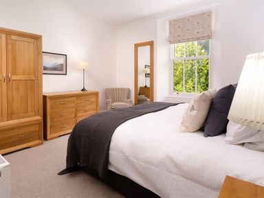 A bedroom with wooden wardrobe and dresser a window and a bed at Ben House in Grasmere