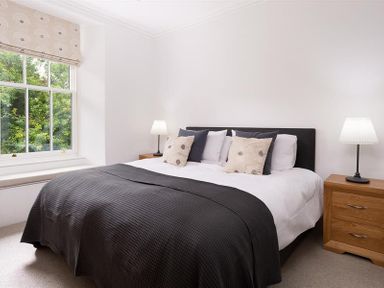 A bedroom with a bed with pillows and a blanket next to a window and bedside tables with lamps at Ben House in Grasmere