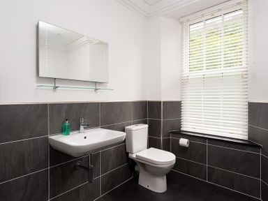 A bathroom with a wall-mounted sink a toilet a mirror and a window with blinds at Ben House in Grasmere