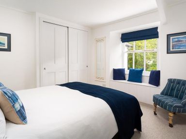 A bedroom with a bed, window seat with cushions, striped armchair, and closet with sliding doors at Ben House in Grasmere