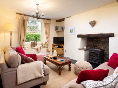 A living room with sofas cushions and a coffee table by a fireplace and window at Birchmill Cottage in Crook
