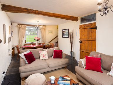 A living room with two beige sofas and red cushions next to a wooden dining table with chairs at Birchmill Cottage in Crook