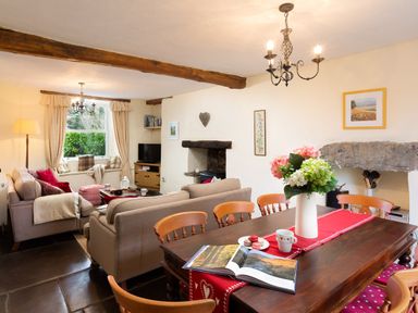 A dining table with flowers and an open book near sofas and a window in a living room at Birchmill Cottage in Crook