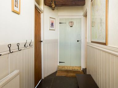 A hallway with a wooden door a light blue door a bench wall hooks and framed pictures at Birchmill Cottage in Crook