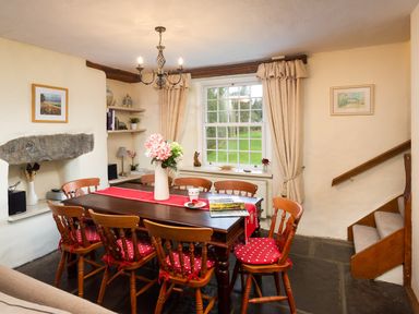A dining room with wooden table and chairs with red cushions and a window at Birchmill Cottage in Crook