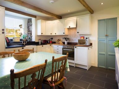 A kitchen with wooden chairs around a table with a teal polka dot tablecloth and white cabinets at Birchmill Cottage in Crook