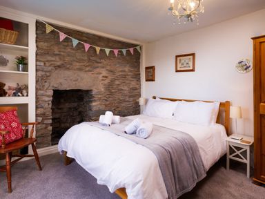 A bedroom with a wooden bed with white bedding and rolled towels a stone fireplace a wooden chair with a red cushion and shelves with toys at Birchmill Cottage in Crook