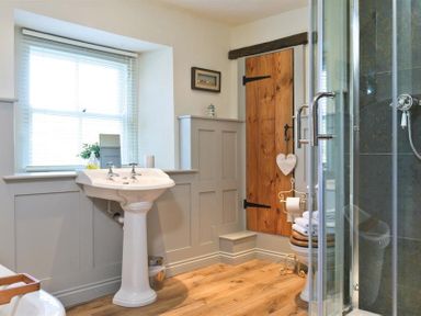 A bathroom with a pedestal sink, wooden door, towel rack, window with blinds and a glass shower at Birchmill Cottage in Crook