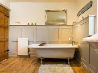 A bathroom with a clawfoot bathtub sink and a wooden door at Birchmill Cottage in Crook