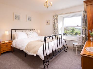A bedroom with a black metal bed frame bedside tables a chair and a window with floral curtains at Birchmill Cottage in Crook
