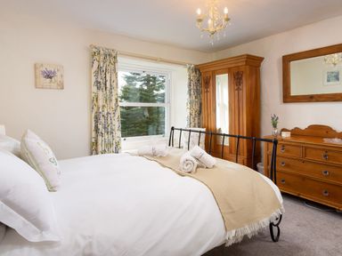 A bedroom with a bed, wooden wardrobe, wooden dresser with mirror, floral curtains, and rolled towels on the bed at Birchmill Cottage in Crook