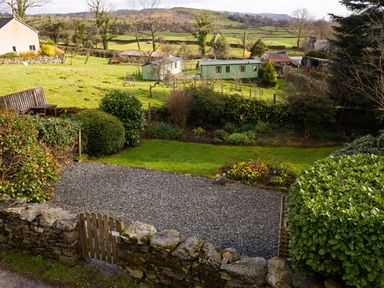 A garden with a gravel area flowers and bushes with green fields and buildings in the background at Birchmill Cottage in Crook