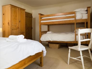 A bedroom with wooden bunk beds a wardrobe a single bed a white chair and folded towels at Birchmill Cottage in Crook