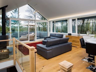 A living room with black leather sofas and large windows overlooking trees at Tall Trees in Bowness