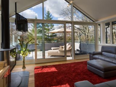 A living room with a red rug leather sofa glass sliding doors and patio furniture at Tall Trees in Bowness