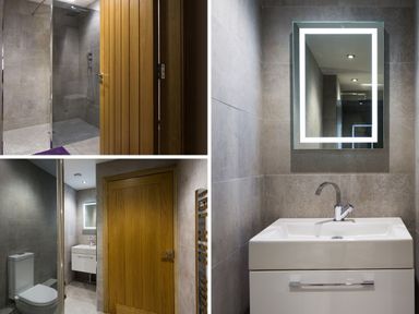 A bathroom with a glass shower area wooden door white toilet and sink with a lit rectangular mirror at Tall Trees in Bowness