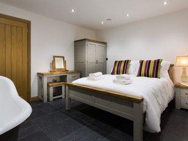A bedroom with a double bed with striped pillows and folded towels a wooden door and furniture and a bathtub at Tall Trees in Bowness