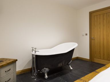 A bathroom with a black clawfoot bathtub a wooden door and a wooden countertop at Tall Trees in Bowness
