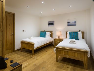 A bedroom with two single wooden beds a wooden nightstand with a lamp and wall art at Tall Trees in Bowness