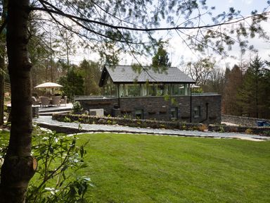 A stone house with a patio and outdoor seating in a garden at Tall Trees in Bowness