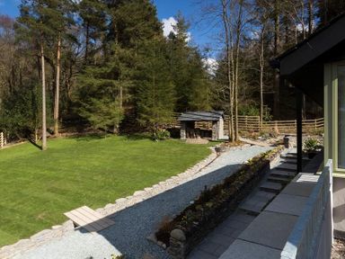 A garden with a grass lawn stone path flower bed and small stone structure at Tall Trees in Bowness