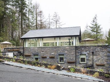 A stone building with windows and umbrellas in a wooded area at Tall Trees in Bowness