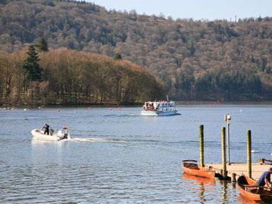 A lake with boats and a dock with trees in the background at Tall Trees in Bowness