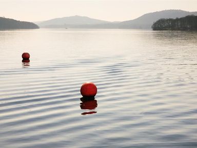 A lake with two red buoys floating on water with hills and trees in the background at Tall Trees in Bowness
